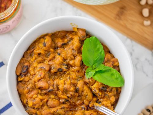 stewed beans in a bowl with a garnish of basil leaves.