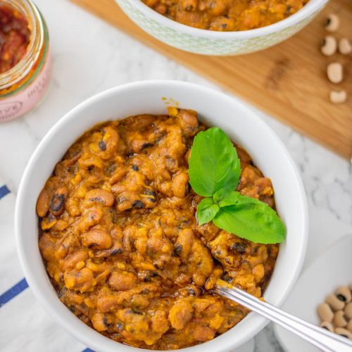 stewed beans in a bowl with a garnish of basil leaves.