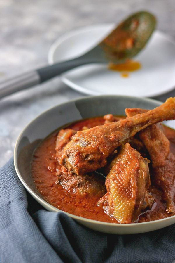 chicken stew served in a grey bowl next to a white plate and serving spoon