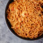 jollof spaghetti and prawns in a black pan.