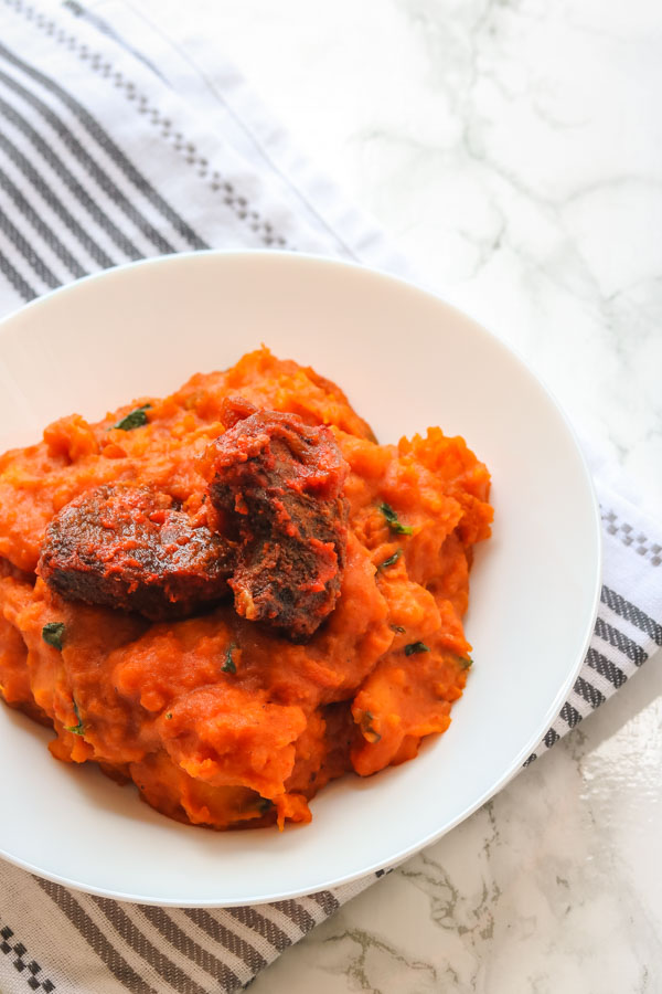 yam porridge and peppered beef served in a white bowl.