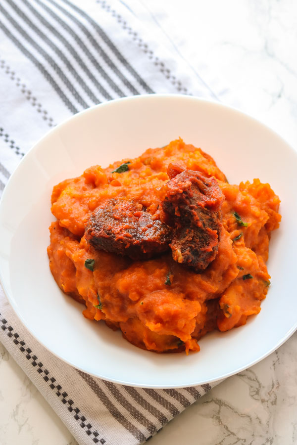 yam porridge and peppered beef served in a white bowl.