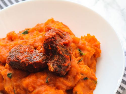 yam porridge and peppered beef served in a white bowl.