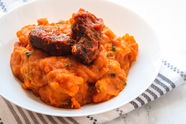 yam porridge and peppered beef served in a white bowl.