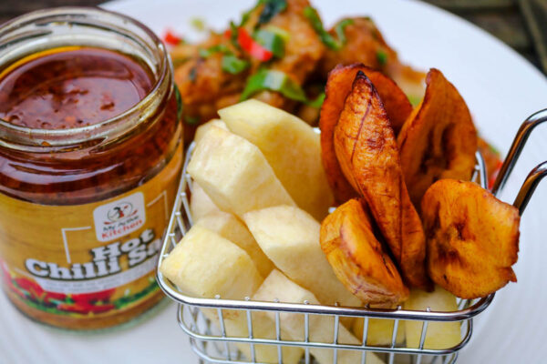 overhead shot of fried yam and plantain with a side of hot chilli sauce on a white plate