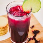 an angled overhead shot of zobo drink garnished with a slice of lime, beside it are stack of cookies