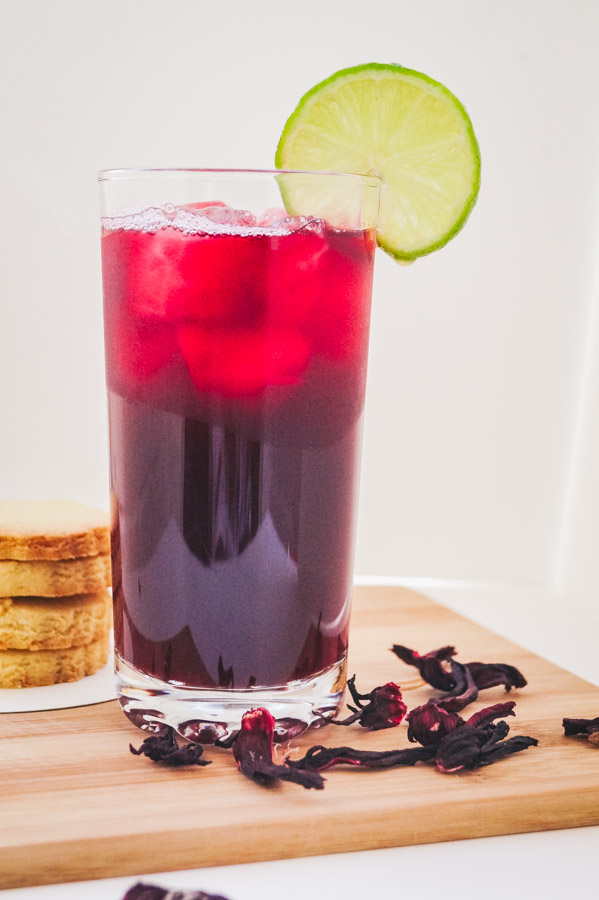 a tall image of hibiscus drink with a garnish of lime rind