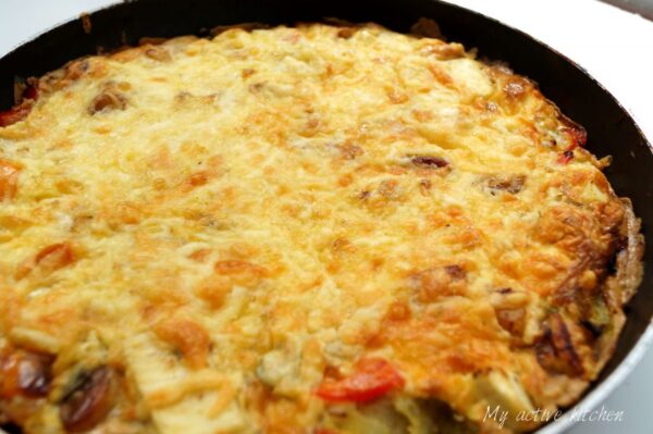 image of uncut plantain frittata still in a pan. Frittata has cheese topping