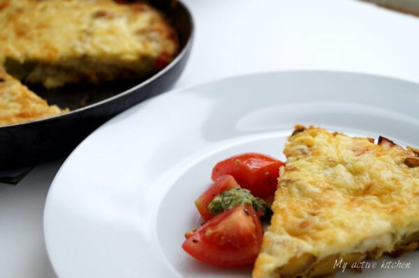 angled shot of frittata wedge served with sliced tomatoes and pesto