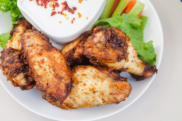 a small plate of easy chicken wings with sliced peppers, lettuce and yogurt dip