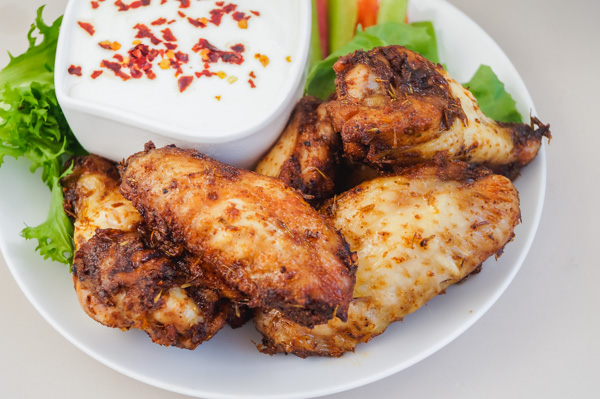a small plate of easy chicken wings with sliced peppers, lettuce and yogurt dip