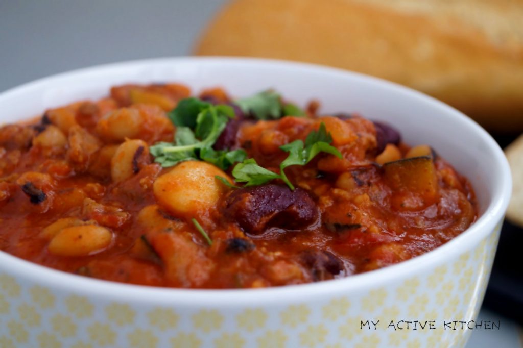 a close shot of bean chilli with a crusty french bread at the background