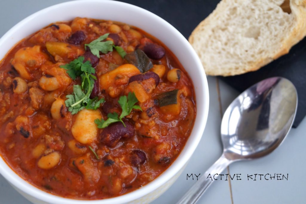 angled overhead shot of 3 bean chilli garnished with parsley and a side of crusty bread