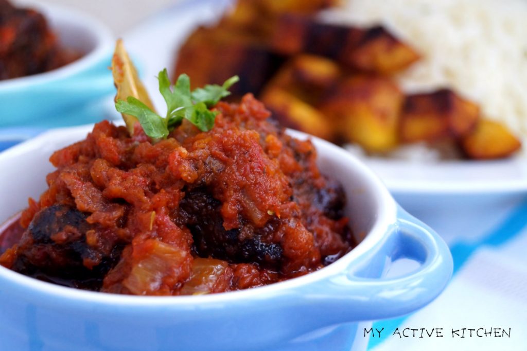 fried stew in blue ramekin. on the side is white plain rice and fried plantain