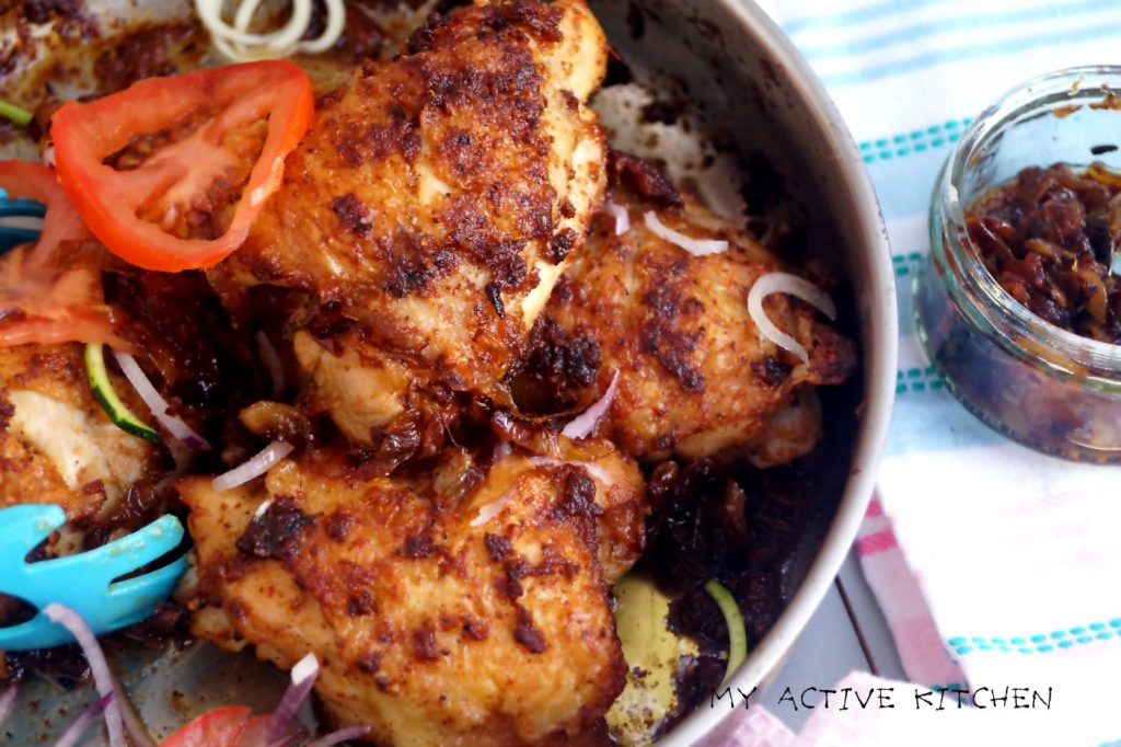 baked chicken suya in a skillet with a side of caramelised onions.