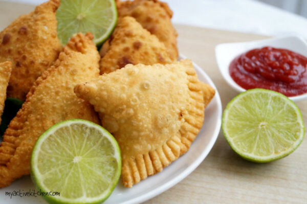 samosa on a white plate with slices of lime and ketchup for dipping