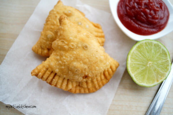 2 samosa's on a white parchment paper with a garnish of lime slice and ketchup for dipping sauce