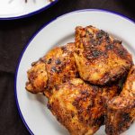 spiced chicken thigh in a white metal plate and a side of salad.