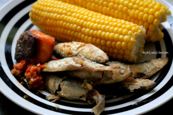 baked salmon and fried smelt fish on a plate with two sweetcorn on hub