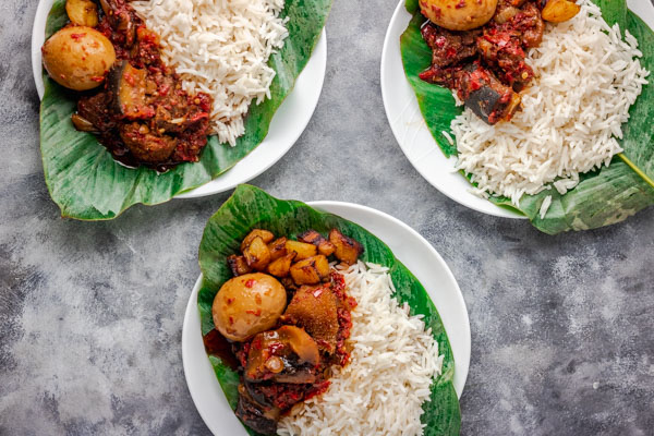 3 plates of ofada stew and plain rice served in a leave placed on white plates.