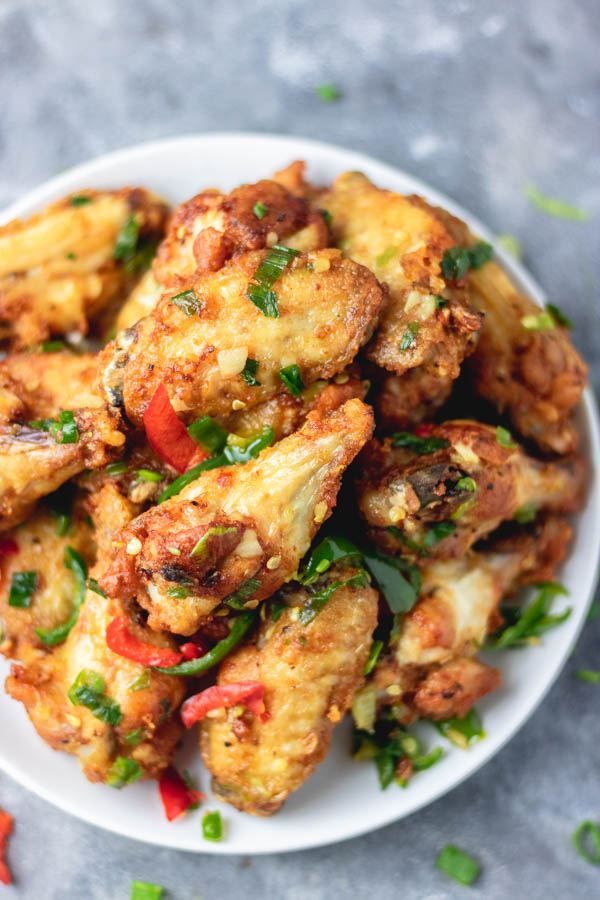 overhead shot of salt and pepper chicken wings on a plate placed on a blue surface.