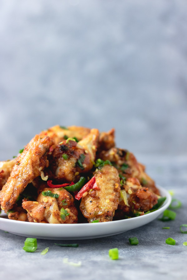 salt and pepper chicken wings on a plate placed on a blue surface.