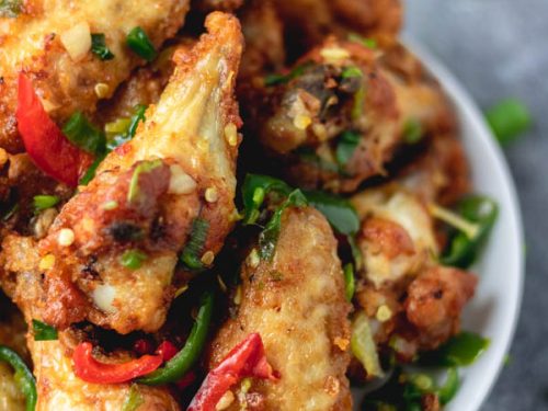 salt and pepper chicken wings on a plate placed on a blue surface.