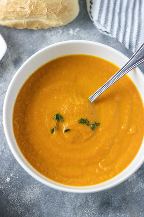 Thick and creamy healthy carrot leek soup served in a bowl and garnished with fresh thyme. Ready to be eaten with a crusty bread roll on the side