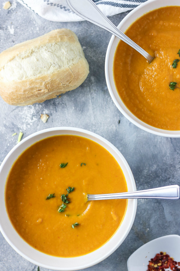Thick and creamy healthy carrot leek soup served in separate two white bowls and garnished with fresh thyme. Ready to be eaten with a crusty bread roll on the side.