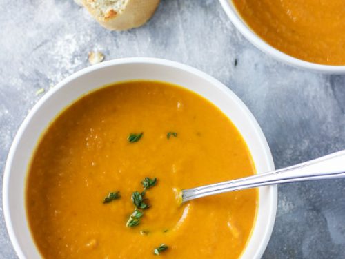 Thick and creamy healthy carrot leek soup served in two white bowls and garnished with fresh thyme. Ready to be eaten with a crusty bread roll on the side