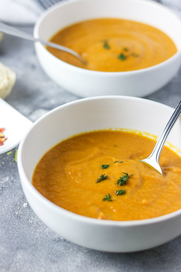 Thick and creamy healthy carrot leek soup served in two white bowls and garnished with fresh thyme. Ready to be eaten with a crusty bread roll on the side