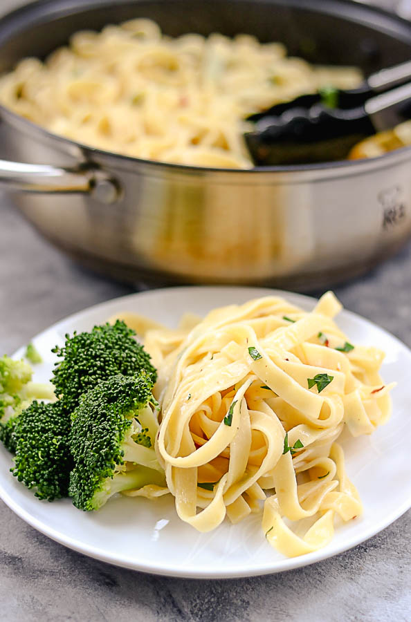 tagliatelle served on a white plate with some broccoli on the side