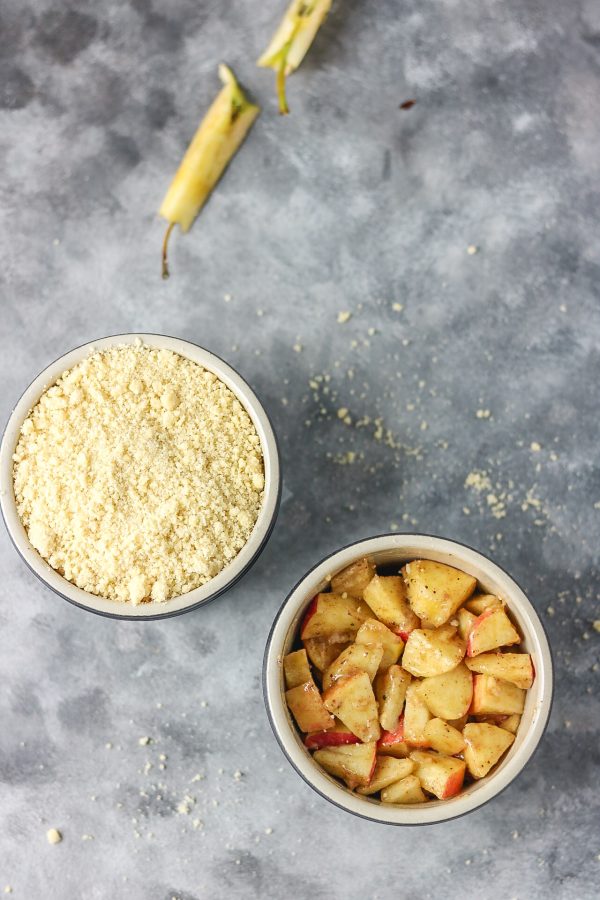 apple crumble in two ramekins. one of the apple crumble image have the toppings while the other have the just apples