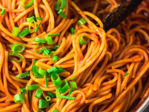 image of cooked pasta still in a pan. pasta is cooked in tomato sauce and garnished with chopped scallions