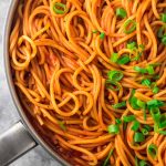 cooked pasta in pan, a black thong is placed on the pasta. the pasta is garnished with chopped pasta and chive