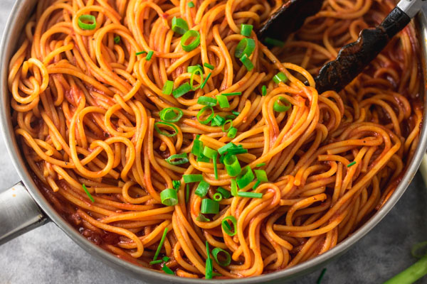 cooked pasta in pan, a black thong is placed on the pasta. the pasta is garnished with chopped pasta and chive 