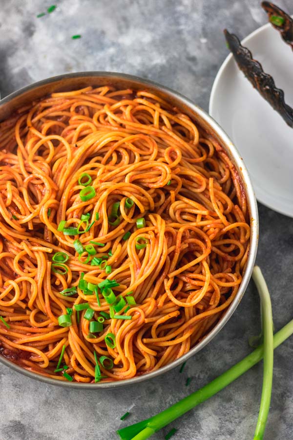 photograph of spaghetti cooked in tomato sauce place beside a white plate and thong