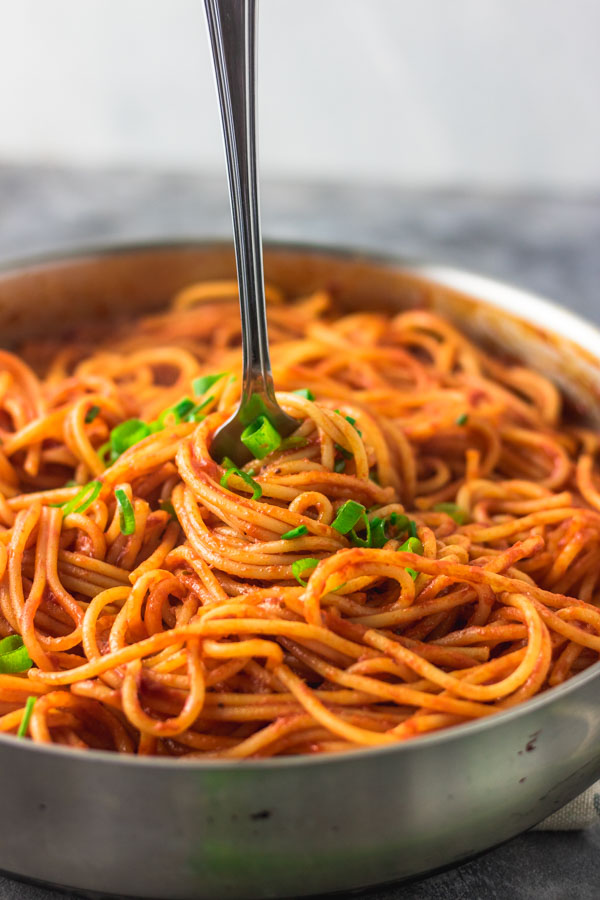 image of a fork in pasta in a pan with garnish of scallions and chives