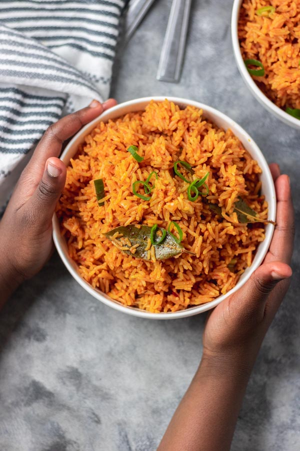 Hands over a bowl of coconut jollof rice