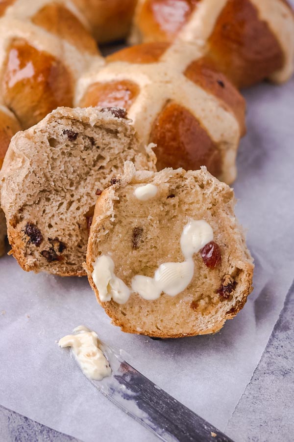 hot cross bun sliced into halves. One half of the bun is slathered with butter.