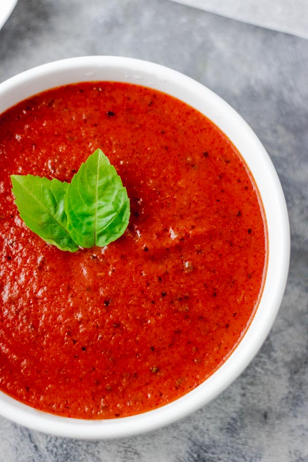 homemade tomato sauce served in a white bowl. the tomato sauce is garnished with basil leaves.