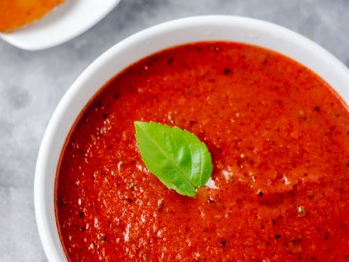 homemade tomato sauce served in a white bowl. the tomato sauce is garnished with basil leaves.