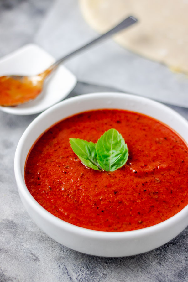 homemade tomato sauce served in a white bowl. the tomato sauce is garnished with basil leaves.