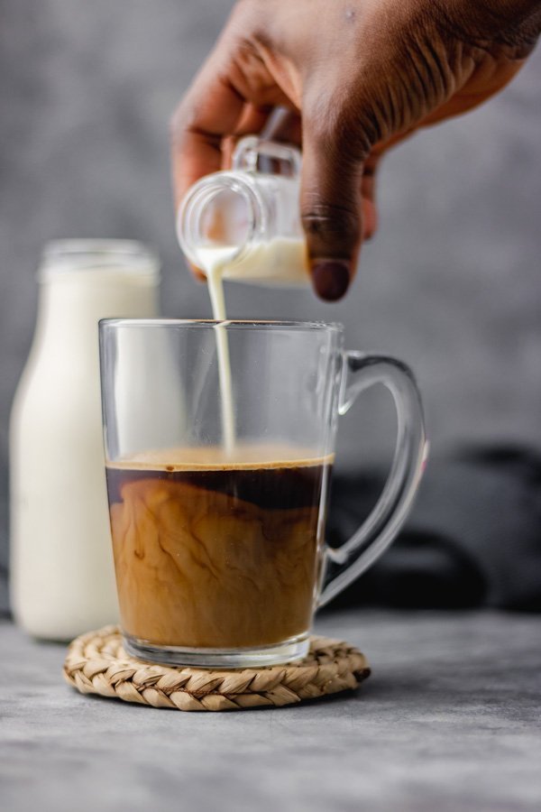 coffee creamer being poured over a cup of coffee. 