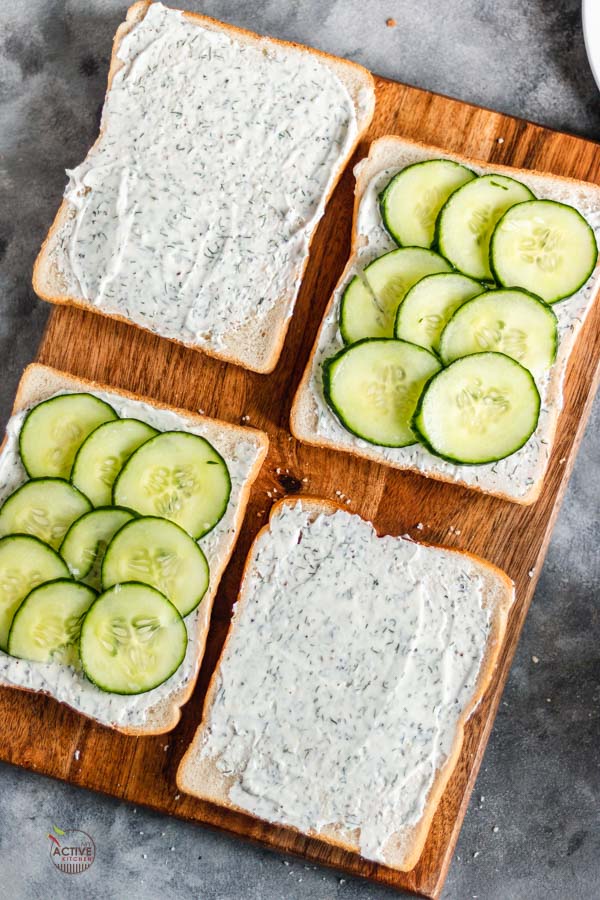 four slices of open cucumber sandwich on a board.
