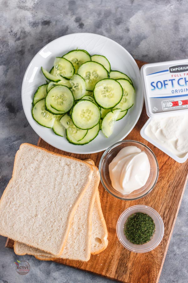 three slices of bread, paper thin cucumber slices on a plate, cream cheese, mayonnaise and dill in small bowl. 