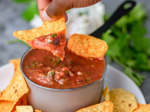 a small hand dipping corn chip into homemade blender salsa.