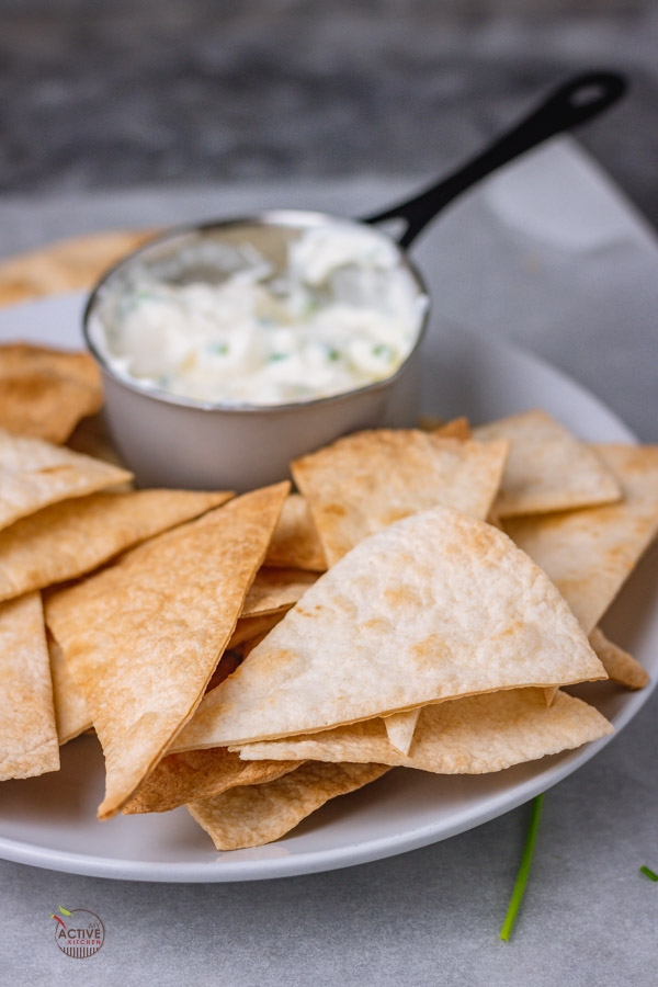 baked flour tortilla chips in a bowl with a side of sour cream and chives dip.