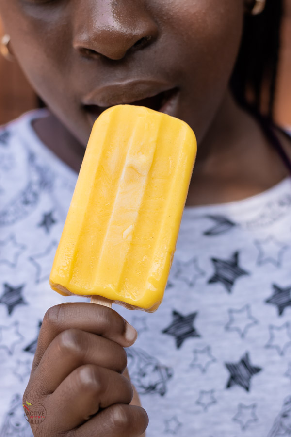 a child holding up a mango Popsicle close to her mouth.