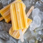 three mango Popsicle and ice on a grey plate.